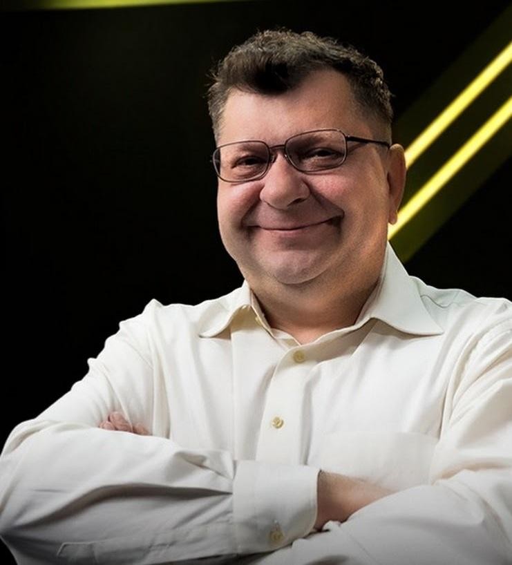 Zbigniew Stonoga w dynamicznej pozie, gestykulujący lub przemawiający, na tle elementów symbolizujących media i działalność publiczną.