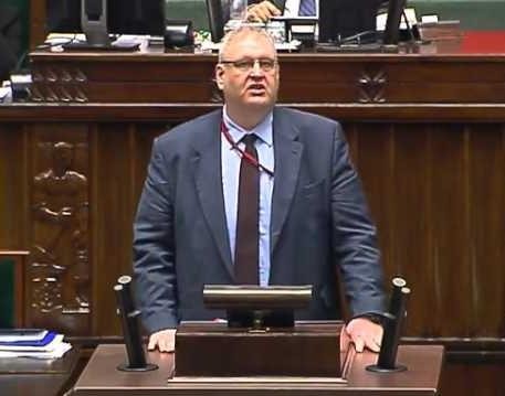 Bogdan Święczkowski w garniturze, na tle instytucjonalnym.